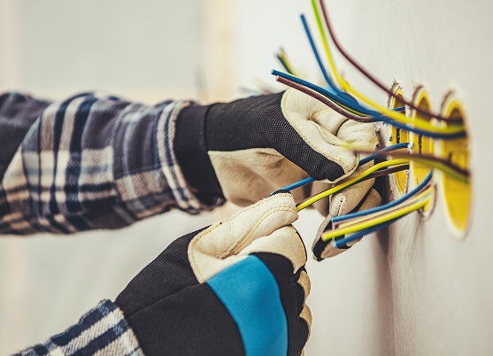 Mains gantées d'un électricien tirant des fils électriques colorés d'une boîte murale. Câblage et installation.