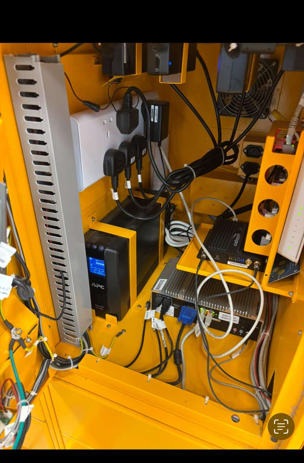 Armoire électrique jaune avec onduleur APC Pro 550, routeur Cradlepoint et câblage industriel organisé.